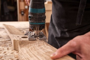 İş kıyafetleri içinde deneyimli bir marangoz ve küçük büstiyer sahibi marangoz, hafif bir atölyede bir testereyle ahşap bir barın kenarlarını gördü ve işledi. 