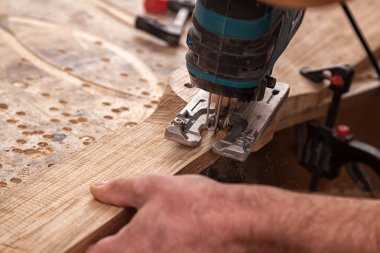 İş kıyafetleri içinde deneyimli bir marangoz ve küçük büstiyer sahibi marangoz, hafif bir atölyede bir testereyle ahşap bir barın kenarlarını gördü ve işledi. 
