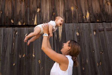 Beyaz bir gömlek güzel esmer kadın bebeği ile oynuyor, kollarını ve ahşap bir çit arka plan gülümseyen holding