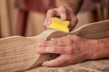 İş kıyafetleri konusunda deneyimli marangoz ve ahşap atölyesinde çalışan küçük büro sahibi atölyede çalışan çocukların helikopter bıçaklarını cilalamak için zımpara kağıdı kullanıyor.  