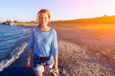 Kot pantolon ve çizgili tişört gülümsüyor, neşeli bir esmer kadın plaj boyunca yürür ve parlak güneşin bir yaz gününde sahiptir. Deniz ve canlı stil yaz tatilleri kavramı