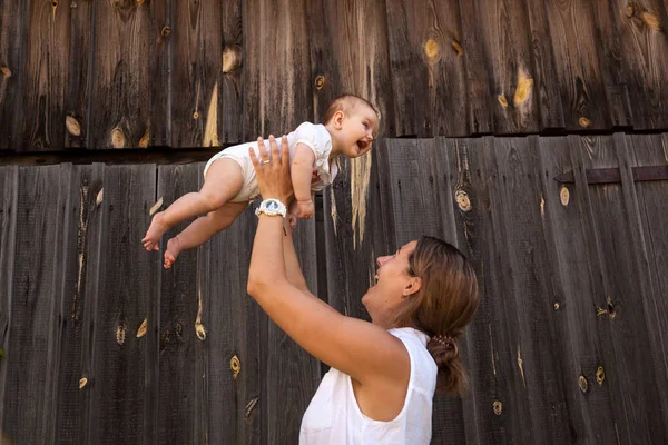 Beyaz bir gömlek güzel esmer kadın bebeği ile oynuyor, kollarını ve ahşap bir çit arka plan gülümseyen holding