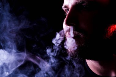 Genç bir adam izole bir siyah kırmızı ve mavi renk renkli duman bulutu exhales. Genç bir hırsız örneği içinde sigara içmek için zarar