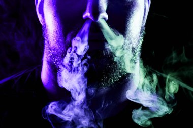 Genç bir adam izole bir siyah mavi ve yeşil renk renkli duman bulutu exhales. Genç bir hırsız örneği içinde sigara içmek için zarar