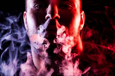 Genç bir adam izole bir siyah kırmızı ve pembe renk renkli duman bulutu exhales. Genç bir hırsız örneği içinde sigara içmek için zarar