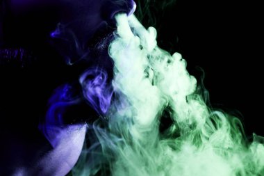 Genç bir adam izole bir siyah kırmızı ve mavi renk renkli duman bulutu exhales. Genç bir hırsız örneği içinde sigara içmek için zarar