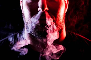 Genç bir adam izole bir siyah kırmızı ve pembe renk renkli duman bulutu exhales. Genç bir hırsız örneği içinde sigara içmek için zarar