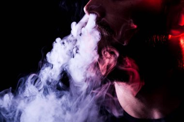 Genç bir adam izole bir siyah kırmızı ve pembe renk renkli duman bulutu exhales. Genç bir hırsız örneği içinde sigara içmek için zarar