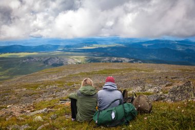 Atmosferik an için dağlarda aşık. Kadın ve erkek sırt çantası ile yürüyüş montaj üstüne oturan ve güzel bir manzara arıyorum. Yaşam tarzı ve yaşam kavramı arka profili seyahat