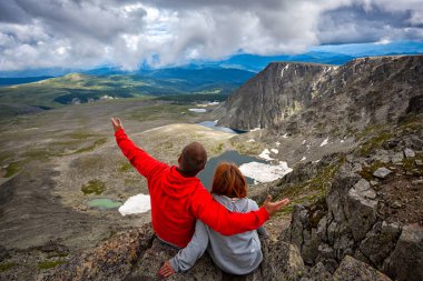 Atmosferik an için dağlarda aşık. Kadın ve erkek sırt çantası ile yürüyüş montaj üstüne oturan ve güzel bir manzara arıyorum. Yaşam tarzı ve yaşam kavramı arka profili seyahat