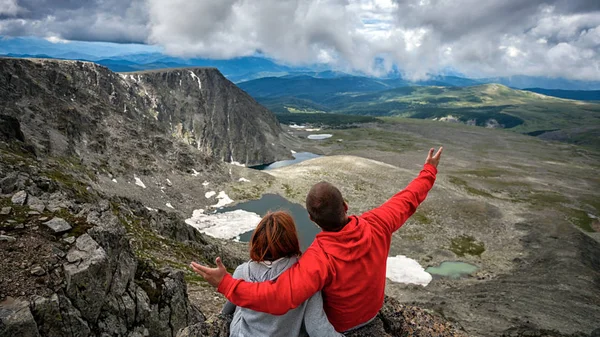 Atmospheric moment for lovers in the mountains.Hiking woman and man with backpack is sitting on the top of the mounting and looking at a beautiful landscape. Travel Lifestyle and survival concept rear view