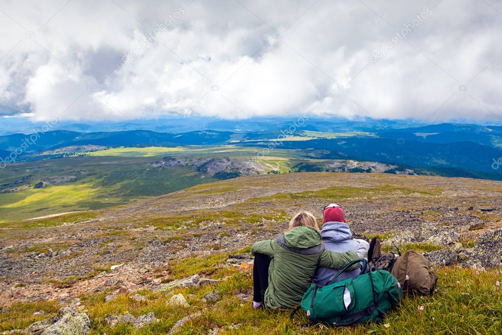 Atmospheric moment for lovers in the mountains.Hiking woman and man with backpack is sitting on the top of the mounting and looking at a beautiful landscape. Travel Lifestyle and survival concept rear view