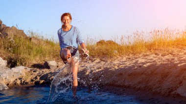Bir neşeli esmer kadın gülümsüyor, plaj boyunca dalgalar başladı, devamlı spreyler ve parlak güneşin bir yaz gününde sahiptir. Deniz ve canlı stil yaz tatilleri kavramı