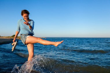 Deniz ve canlı stil kavramı yaz tatilleri. Bir genç esmer kadın gülümsüyor, plaj boyunca dalgaları ile oynamak, çünkü çok spreyler ve parlak güneşin bir yaz gününde sahiptir. 