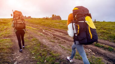Yaşam tarzı ve yaşam kavramı arka profili seyahat. Kadınlar trekking zevk sırt çantası ile hiking, arka planda dağlar dağlar yeşil bir alana gidin. Güneş parlıyor, sıcak yaz gününde mavi gökyüzü.