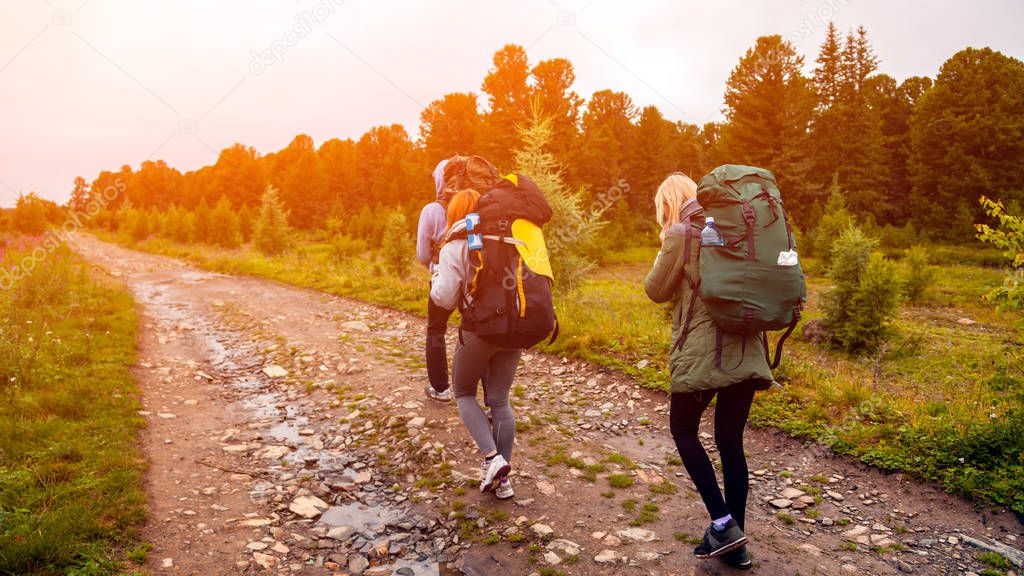 Travel Lifestyle and survival concept rear view. Two  hiking women with backpack go along the path to the mountains in a long hike on a warm summer day, a back view.