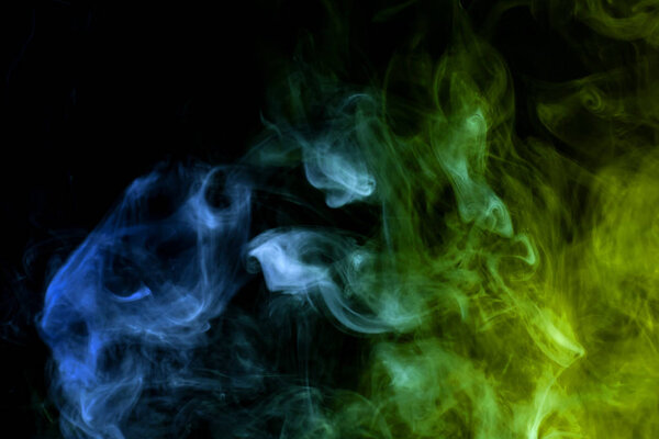 Thick colorful blue, green and yellow smoke on a black isolated background. Background from the smoke of vap