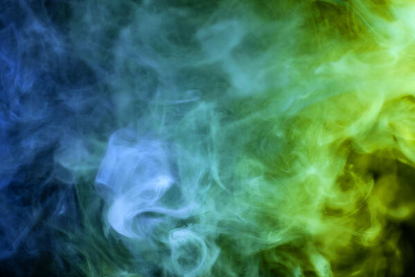 Dense multicolored smoke of blue and green colors on a black isolated background. Background of smoke vap