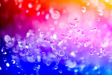 Yakın yukarı bir su damlaları üzerinde kırmızı, yaellow ve mavi degrade arka plan ile kaplı, damla su - yoğunlaşma. Yakın çekim yukarı doğru uçan bir çeşme bir damla