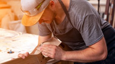 İş kıyafetleri konusunda deneyimli marangoz ve ahşap atölyesinde çalışan küçük büro sahibi atölyede çalışan çocukların helikopter bıçaklarını cilalamak için zımpara kağıdı kullanıyor.  