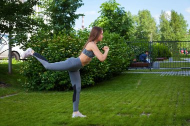 Esmer kadın at arabasıyla bir sportif kısa üst ve spor salonu tozluk lunges tarafında yapar, yeşil çim üzerinde bir parkta bir yaz gününde onun ellerini onun önünde tutar