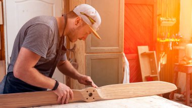 İş kıyafetleri konusunda deneyimli marangoz ve ahşap atölyesinde çalışan küçük büro sahibi atölyede çalışan çocukların helikopter bıçaklarını cilalamak için zımpara kağıdı kullanıyor.  