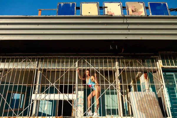 Young woman looking from behind bars. trapped woman behind iron bars. Young sporty  woman in blue swimsuit enjoying a summer day and posing  against the background of a mettalic fence.