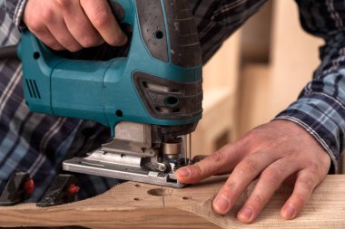 İş kıyafetleri içinde deneyimli bir marangoz ve küçük büstiyer sahibi marangoz, hafif bir atölyede bir testereyle ahşap bir barın kenarlarını gördü ve işledi. 