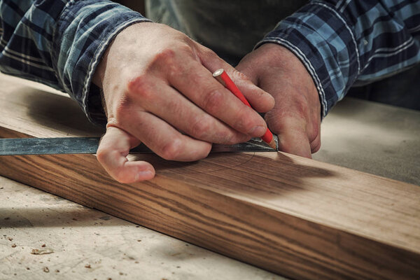 Close-up The man measures a wooden board with a ruler and marks with pencil the necessary points for slices