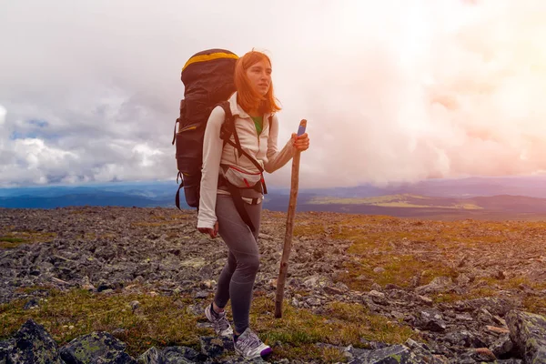 Atmospheric moment in mountains. Hiking woman with backpack traveler on top of mountains. Stylish woman hiking, in the background a green forest, field and high mountain