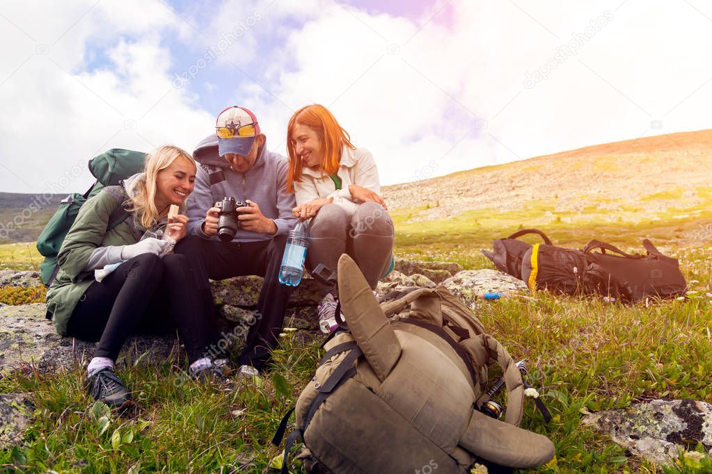 Travel Lifestyle and survival concept rear view. Hiking man and women with backpack enjoys a hike  and looks at the pictures taken on  camera in the mountains in the background a green floor and cloud. Photographer traveler on  high mountaint. Wander