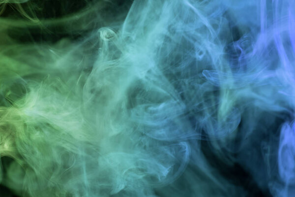 Dense multicolored smoke of   blue and green colors on a black isolated background. Background of smoke vap