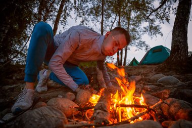 Genç turist çadır ve orman arka planda kamp yemek hazırlamak için bir yangın esiyor. Yaşam tarzı ve yaşam kavramı arka profili seyahat