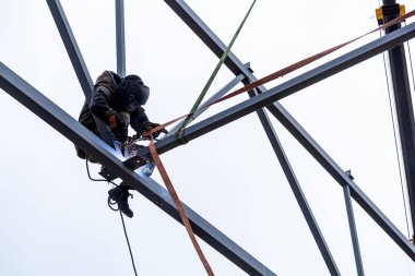 Yükseklik maskesi kaynak sigorta ile çalışan bir adam Kaynakçı Kaynak metali metal bir yapı mavi gökyüzüne karşı bir irtifada oturuyor ve var