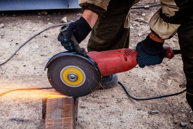 Güçlü adam kaynakçı kahverengi üniforma, kaynakçılar deri, değirmeni metal inşaat sahasında turuncu kıvılcım sinek iki yanda bir açı değirmeni yakın çekim
