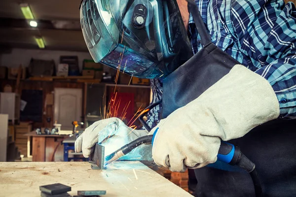 Kaynak maskesi ve kaynakçılar deri bir genç adam kaynakçı üniformalı, yakın çekim, atölye, mavi ve turuncu kıvılcım sinek iki yanda makinesinde ark ile metal kaynak