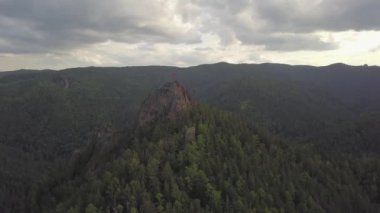 Hava dron görüntüleri İzlenme: Havadan görünümü uçuş uçuş yüksek dağların üzerinde yeşil iğne yapraklı çam ağaçları ve cedars ile kaplı. At dağın zirvesine tırmanış onuruna ayarla bayrağı, büyük bir kaya türü.