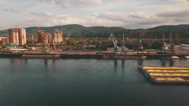 空中ドローン映像ビュー 空撮フライト バック グラウンドで川の貨物 建設クレーンを台船に山川の上の近代都市と公園 川の貨物船 — ストック動画