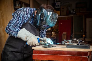 Maske ve kaynakçılar deri, kaynak bir genç adam kaynakçı üniformalı, Kaynak metali ile atölye, mavi ve turuncu kıvılcım sinek iki yanda makinesinde ark