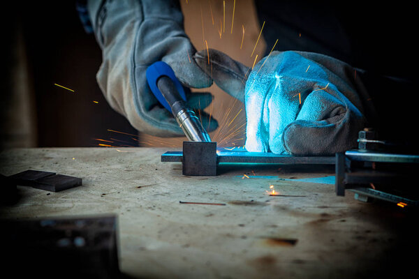 Strong man welder in work clothes hard working and welds with a welding machine metal