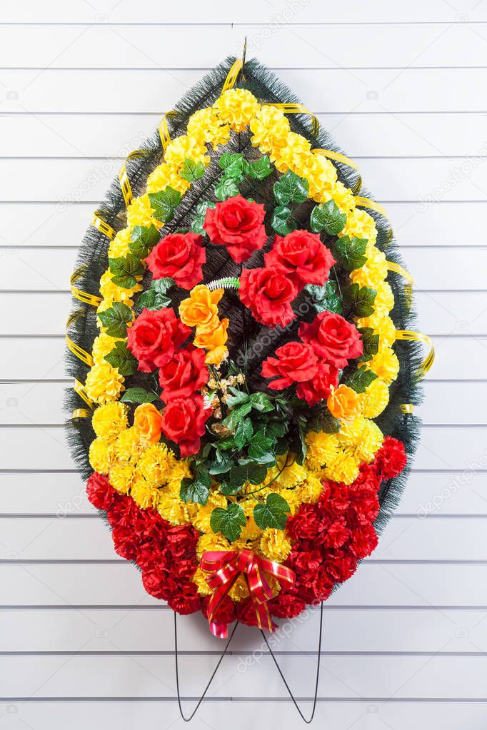 Luxury funeral wreath with red and yellow flowers on a white striped isolated background
