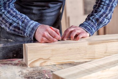 Yakından bakınca, adam cetvelle ahşap bir tahta ölçer ve dilimler için gerekli noktaları kalemle işaretler.