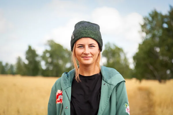 Young woman in green coat, knitting hat, jeans walking, enjoying nature and sunlight in straw field. Concept of autumn  holidays at village  and live style