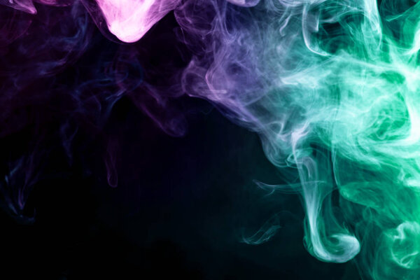 Dense multicolored smoke of pink, blue and green colors on a black isolated background. Background of smoke vap