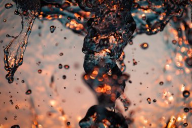 Su damla bir sürü jetler ve sarı-turuncu arka plan üzerinde güneşin altında kabarcıklar. Büyük planı büyük çeşmeden su dalgaları doku