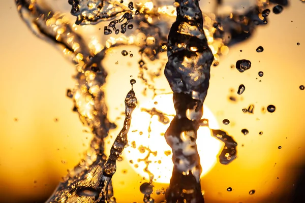 液滴と黄色オレンジ色の背景に太陽の下で気泡と水のストリームのクローズ アップ 大きな噴水の水の波の質感 — ストック写真