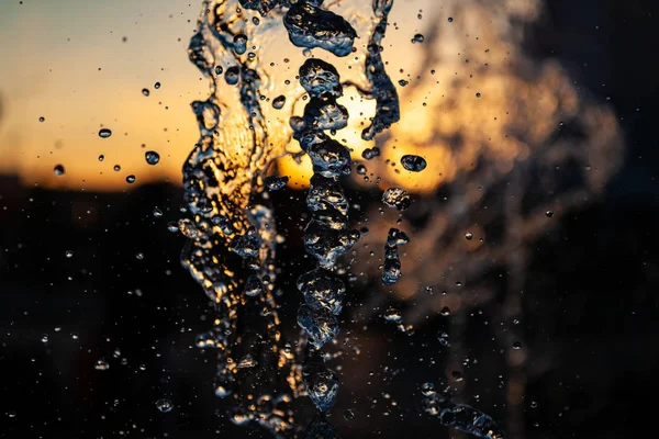 多くの滴と水のジェット オレンジ色の背景に太陽の下で泡します 大きな噴水の水の波の質感の大計画 — ストック写真