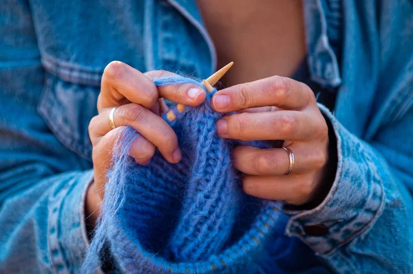 A young woman in a jeans jacket and  knitting hat with needle and natural wool on the back of the background is the autumn landscape of the field.Concept of a freelancer work in the open air