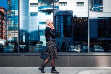 Mavi örgü şapka ayakta yapmak büyük şehirde sonbahar güneşli arka plan ayna duvar çalışması için güzel bir genç model portresi. Sonbahar sıcak fotoğraf. Kadın gülümsüyor ve göz uzak, neşeli neşeli ruh.