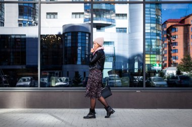 Mavi örgü şapka ayakta yapmak büyük şehirde sonbahar güneşli arka plan ayna duvar çalışması için güzel bir genç model portresi. Sonbahar sıcak fotoğraf. Kadın gülümsüyor ve göz uzak, neşeli neşeli ruh.